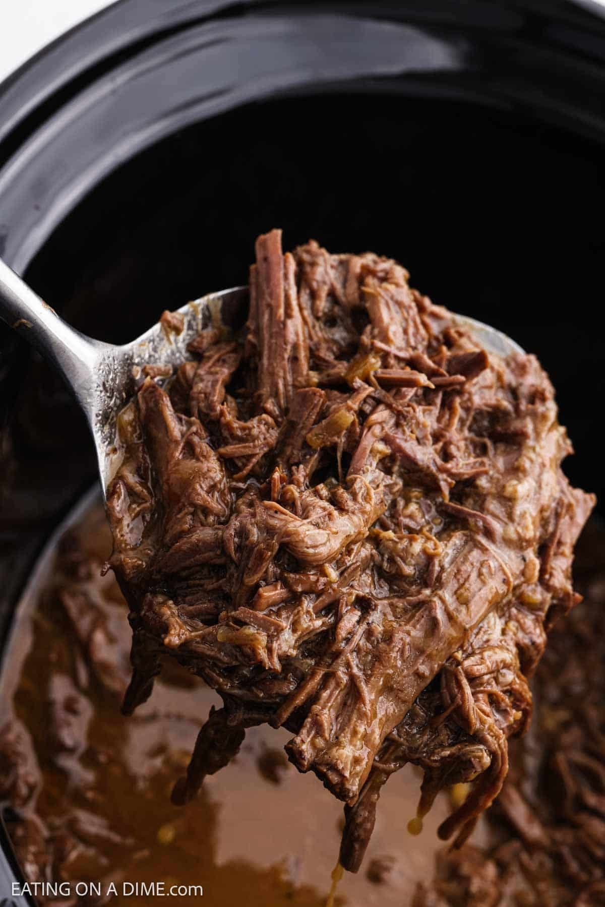Shredded beef on a spoon over a crockpot.