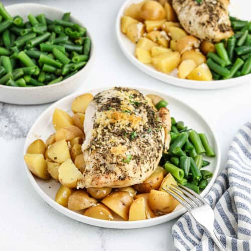 Seasoned chicken breast on cut potatoes and green beans on a plate.