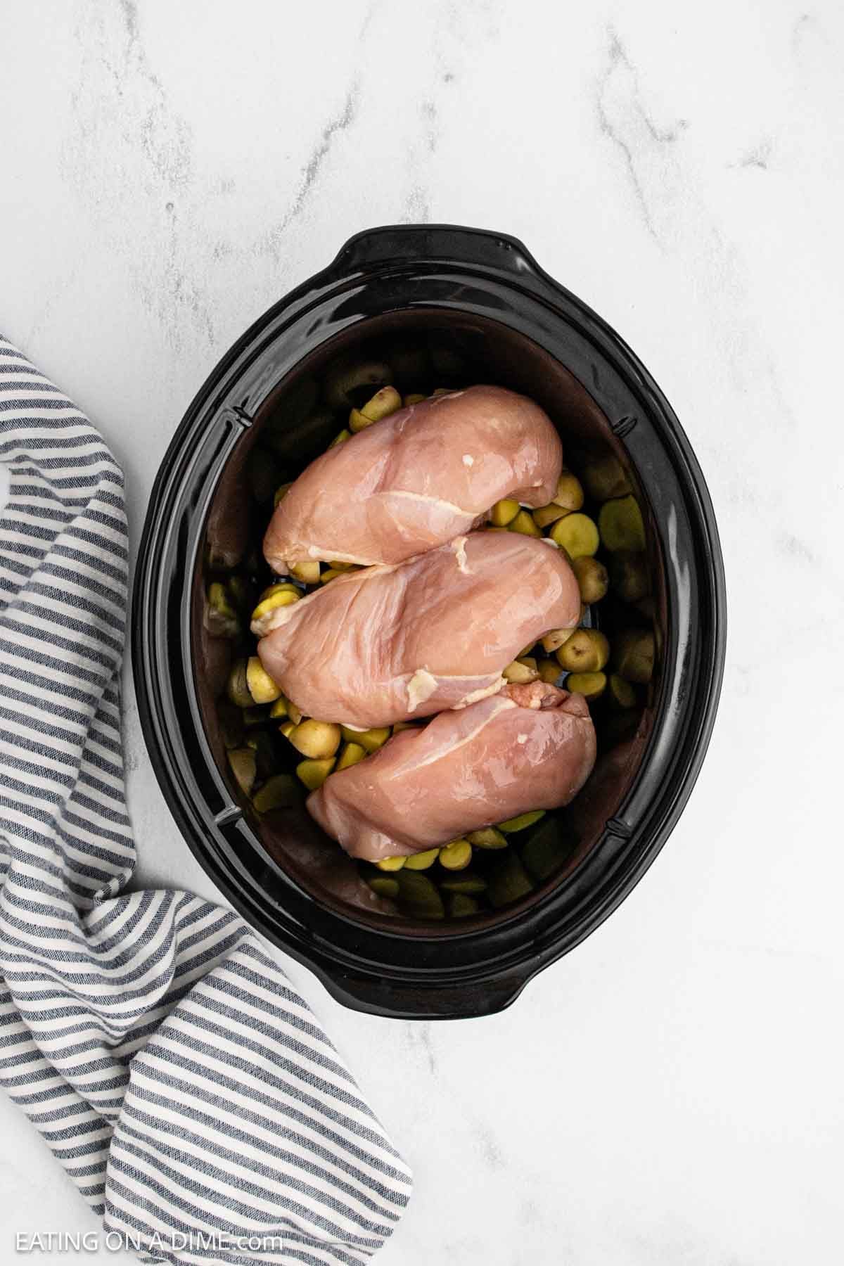 Raw chicken breasts are placed on diced potatoes in the crock pot.