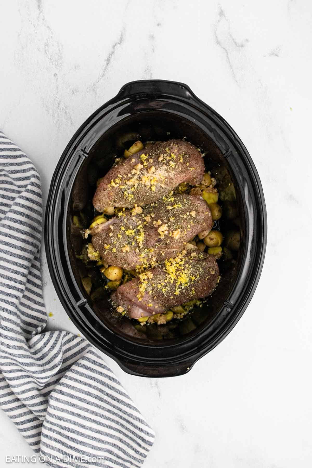 Minced garlic sprinkled over the seasoned raw chicken breast over diced potatoes in the crockpot.