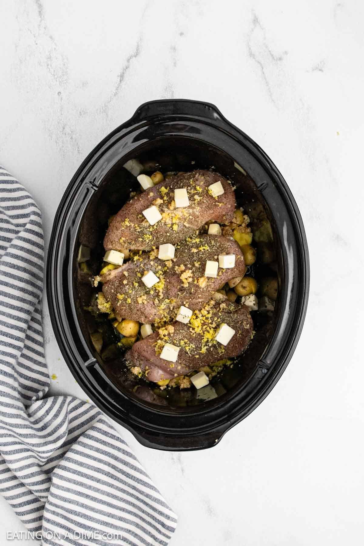 Diced butter sprinkled over the seasoned raw chicken breasts over the diced potatoes in the crockpot.