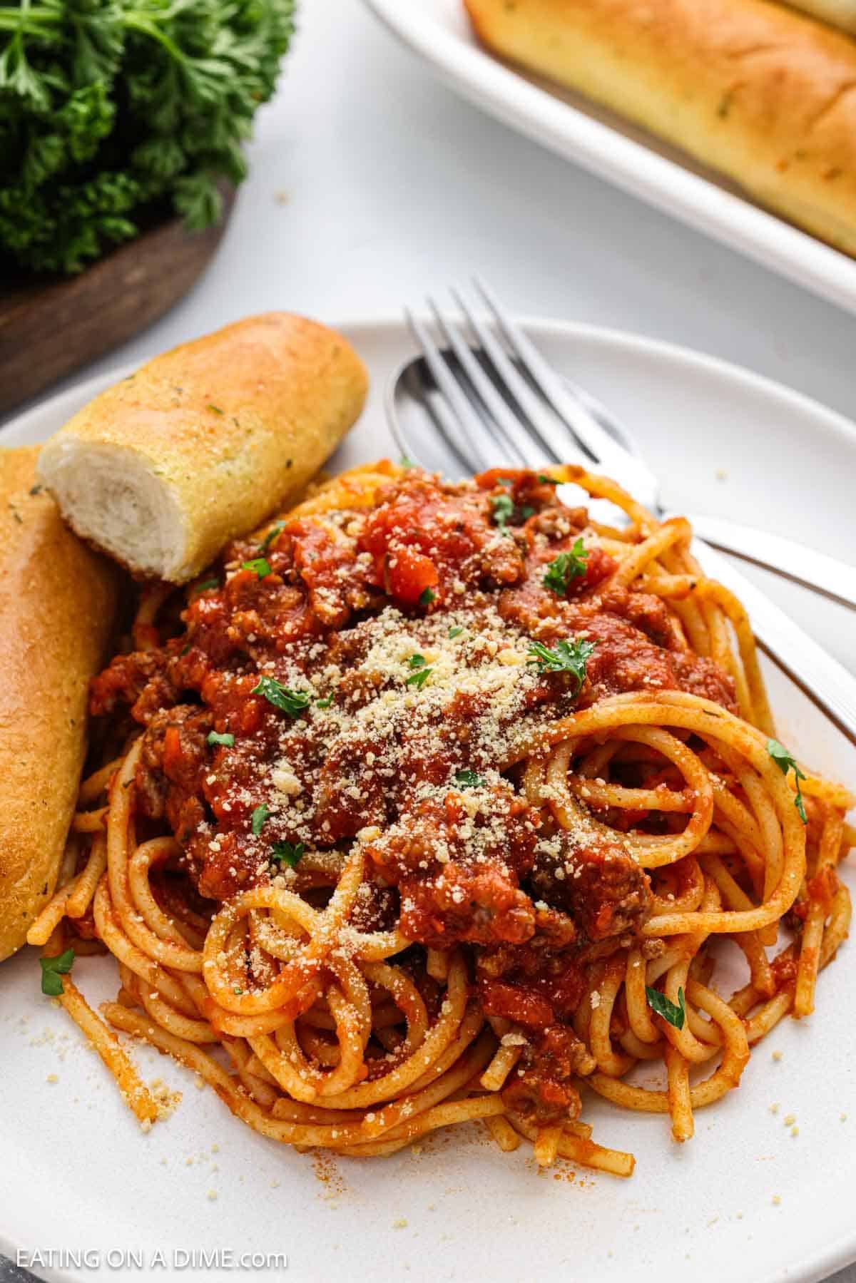 A serving of spaghetti on a plate with a bread sticks.