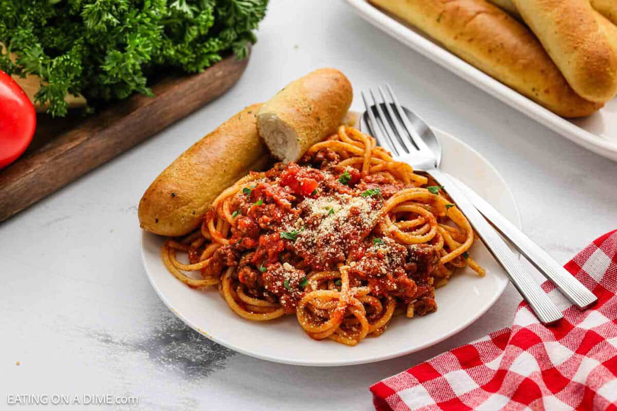 Spaghetti on a plate with breadsticks on the side.