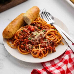 A serving of spaghetti on a plate with a side of breadsticks.