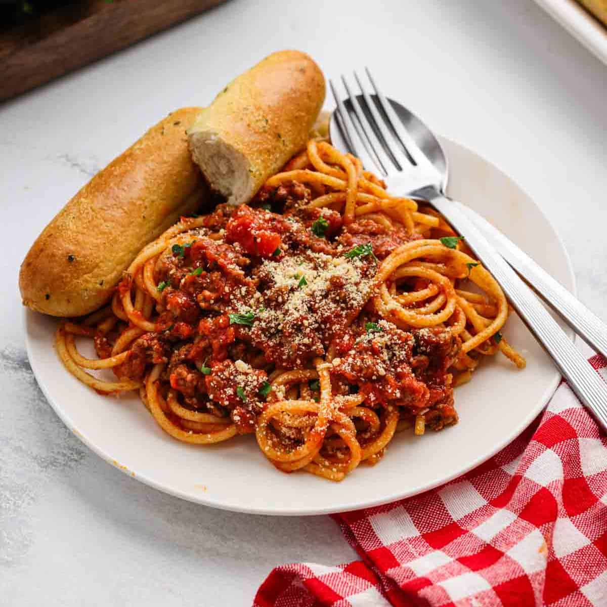 A serving of spaghetti on a plate with a side of breadsticks.