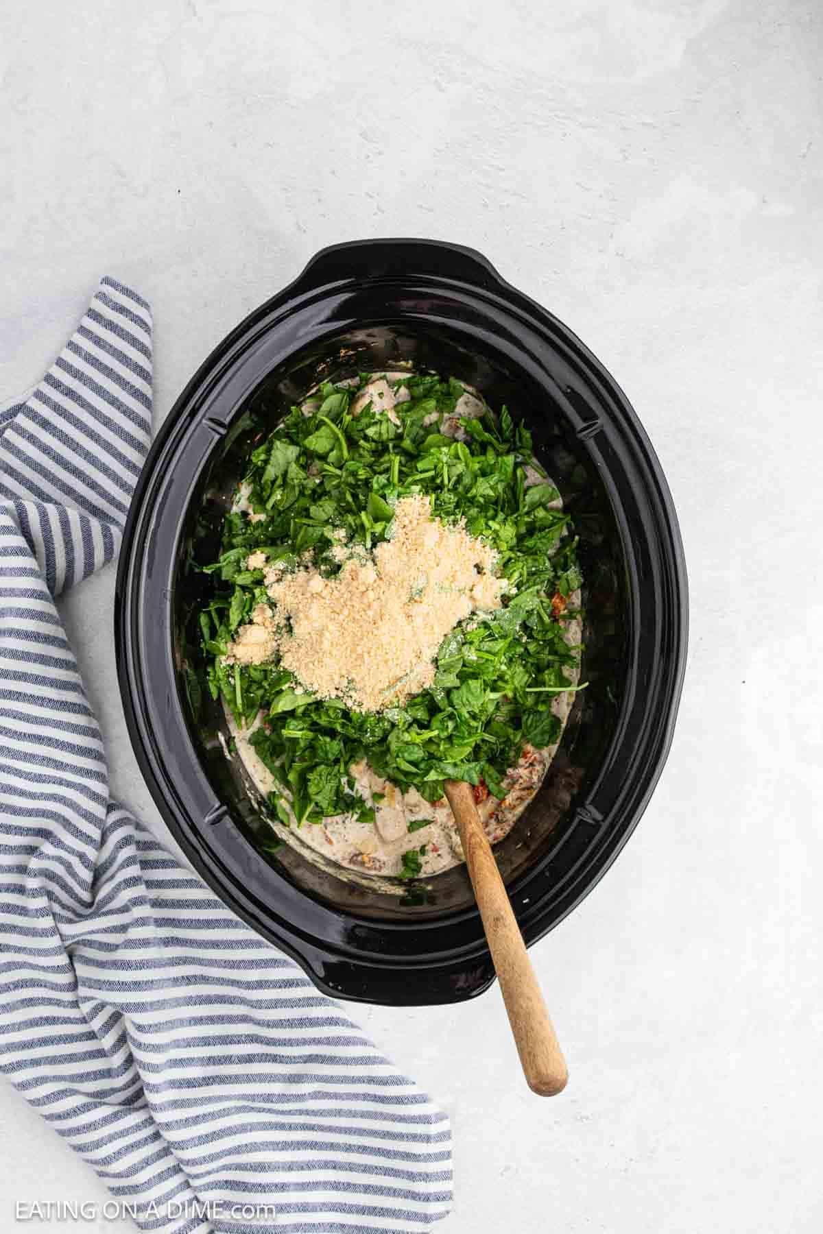 Parmesan cheese and spinach added to the creamy ingredients in the crock pot.