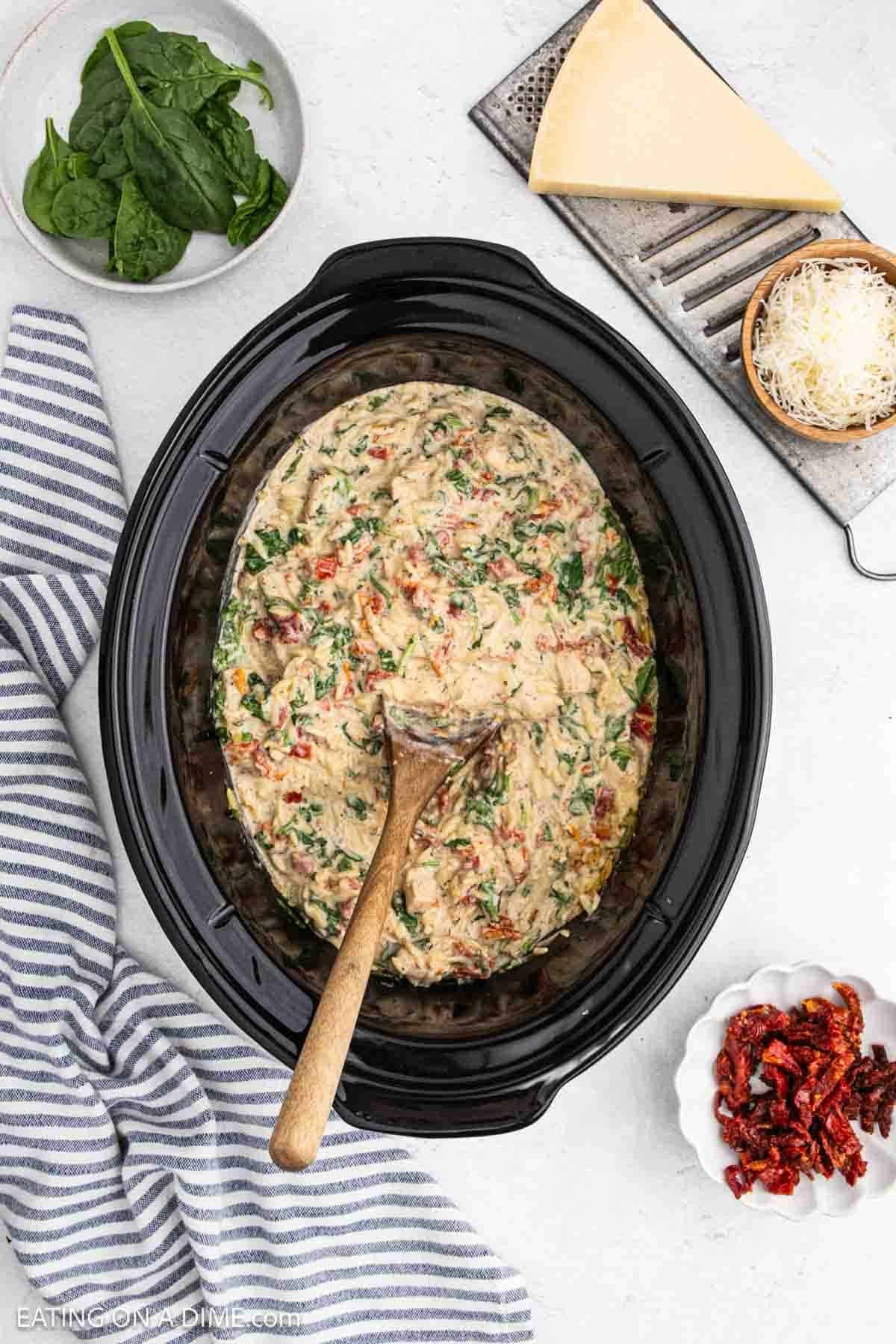 Chicken Orzo in the crock pot with a wooden spoon placed in the mixture.