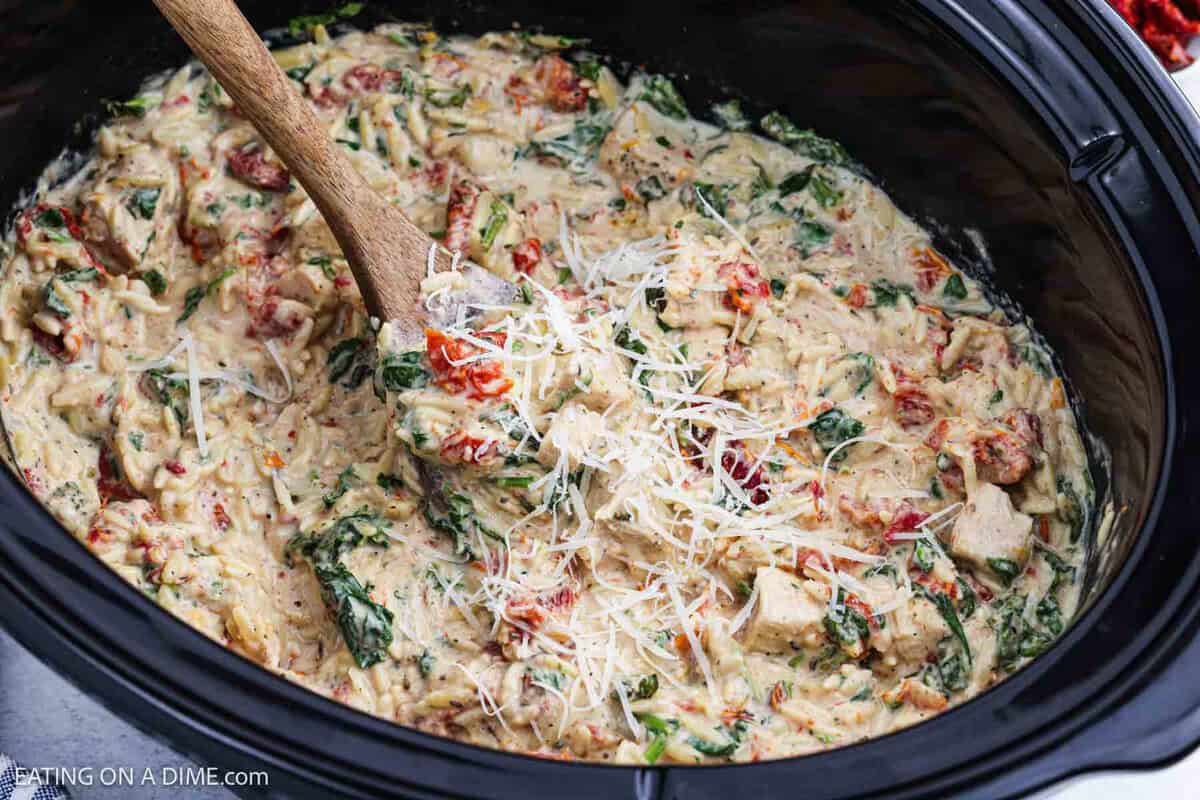 Chicken Orzo in the crockpot with a wooden spoon taking out a serving.