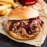 Pulled pork sandwich topped with BBQ sauce with a side of French Fries.