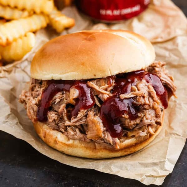 Pulled pork sandwich topped with BBQ sauce with a side of French Fries.