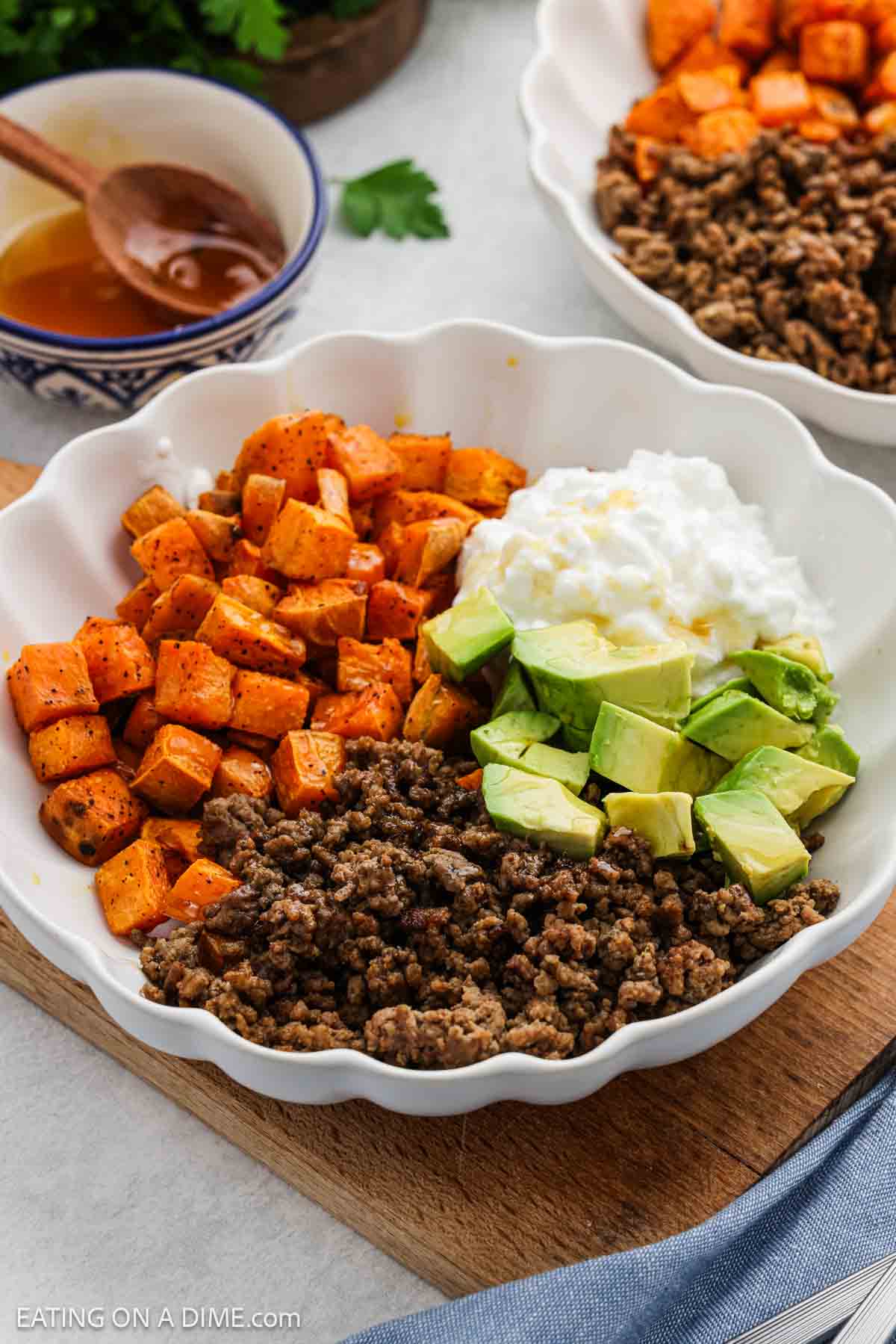 Cooked ground beef, diced sweet potatoes, cottage cheese and diced avocados in a white bowl.