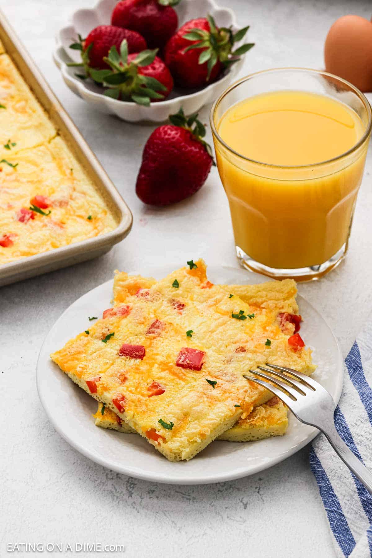 Cooked eggs cut into squares stacked on a small plate with a glass of orange juice nearby.