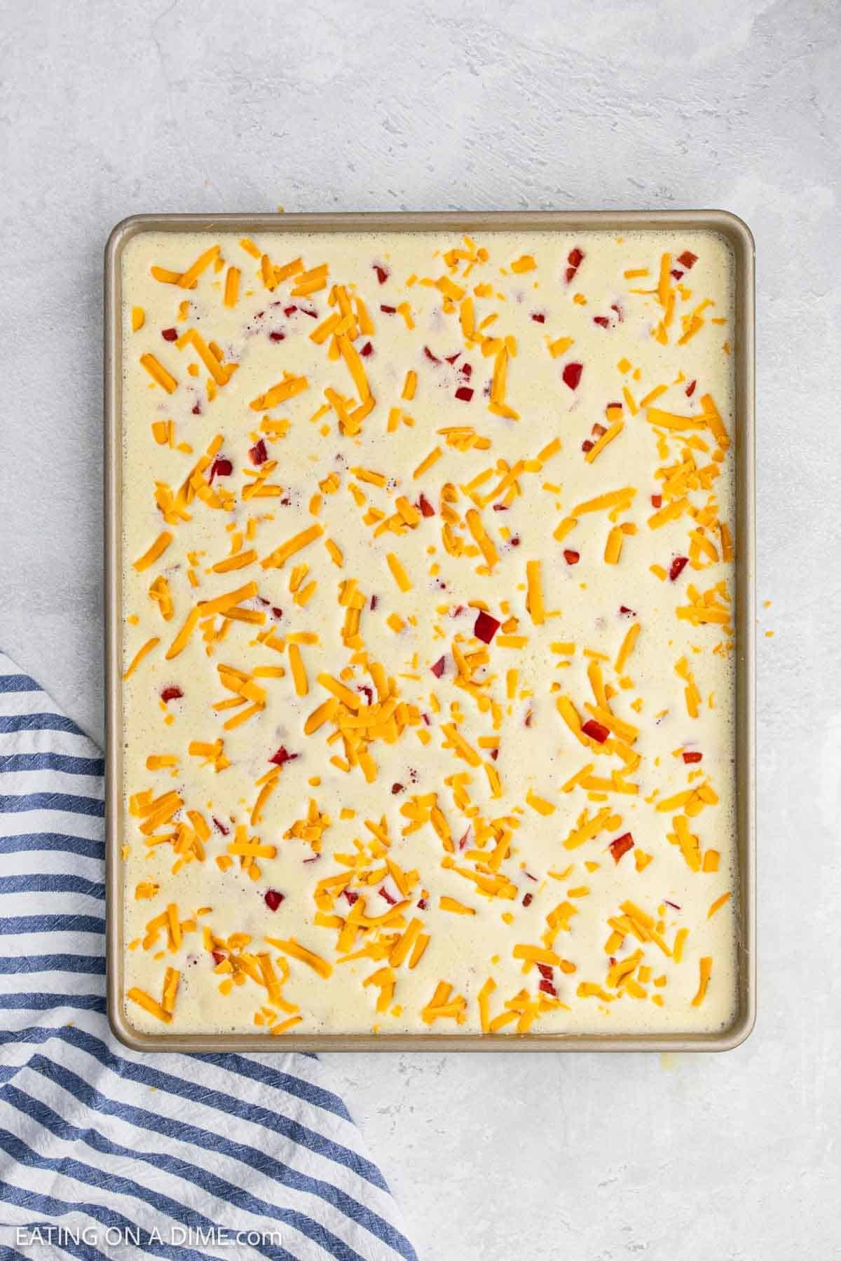 Egg mixture in the sheet pan topped with shredded cheese and red bell pepper.