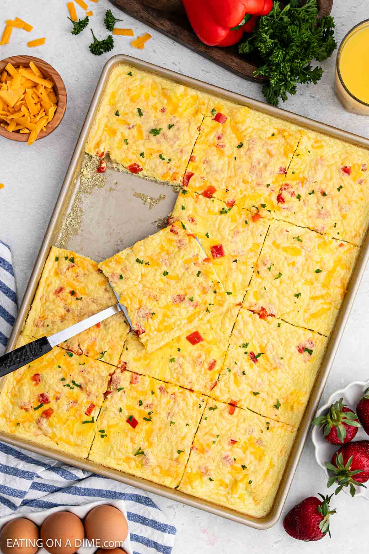 Baked eggs with melted cheese and red bell peppers cut into squares with a serving on a spatula in a sheet pan.