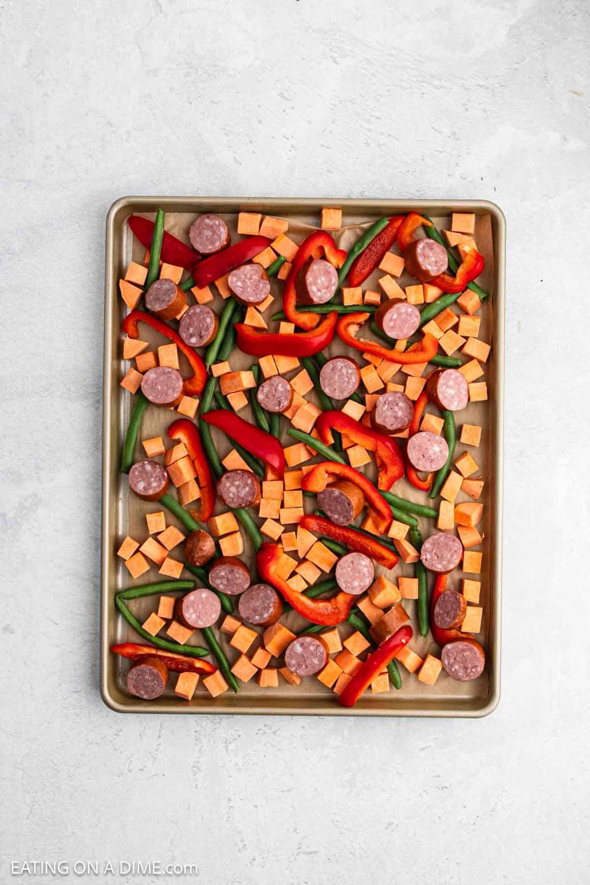 Sliced sausage placed on the baking baking sheet with the chopped vegetables.