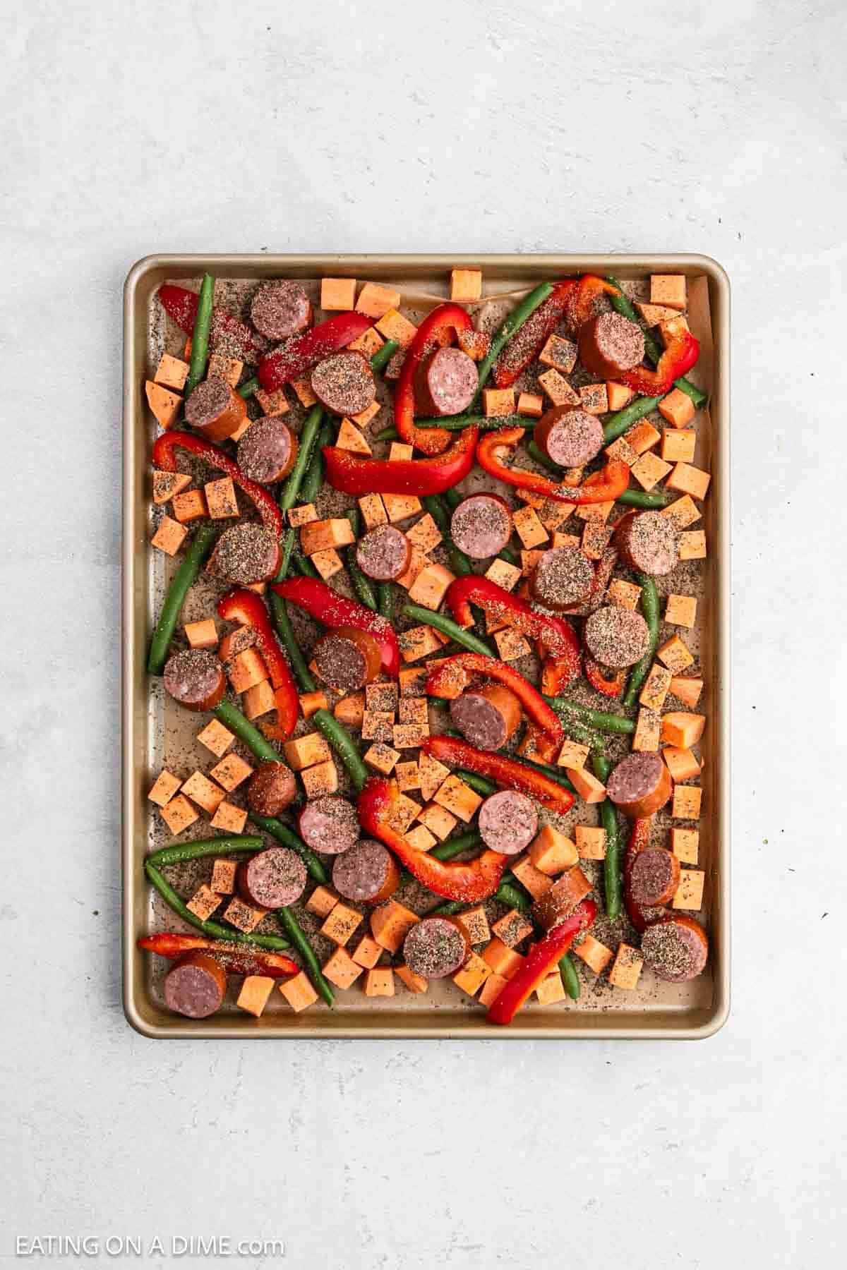 Seasoning mixture sprinkled over the slice sausage and chopped veggies on a baking sheet.