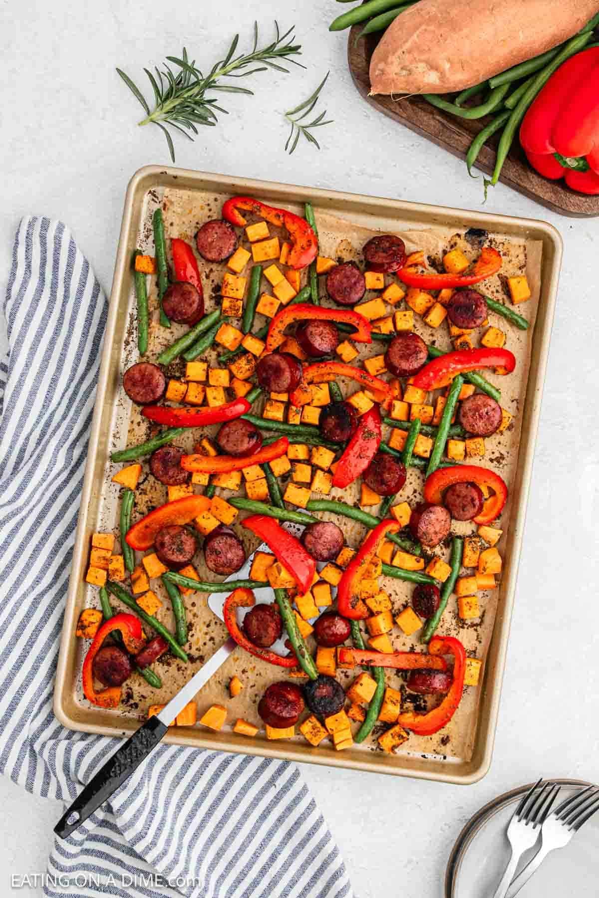 Roasted sliced sausage and chopped veggies on a baking sheet.