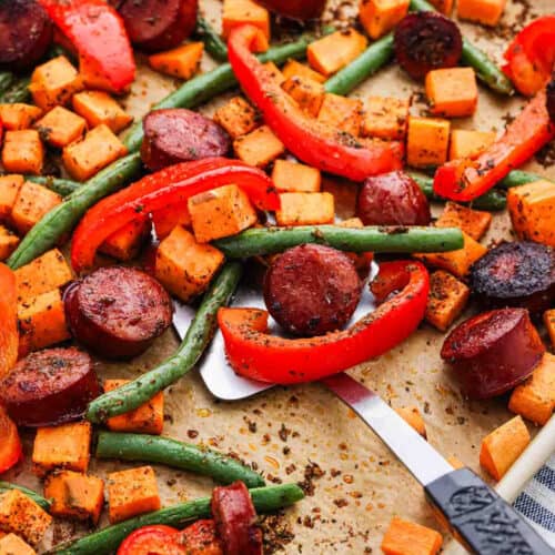 Sliced sausage, diced sweet potatoes, red bell peppers, and green beans on a baking sheet.