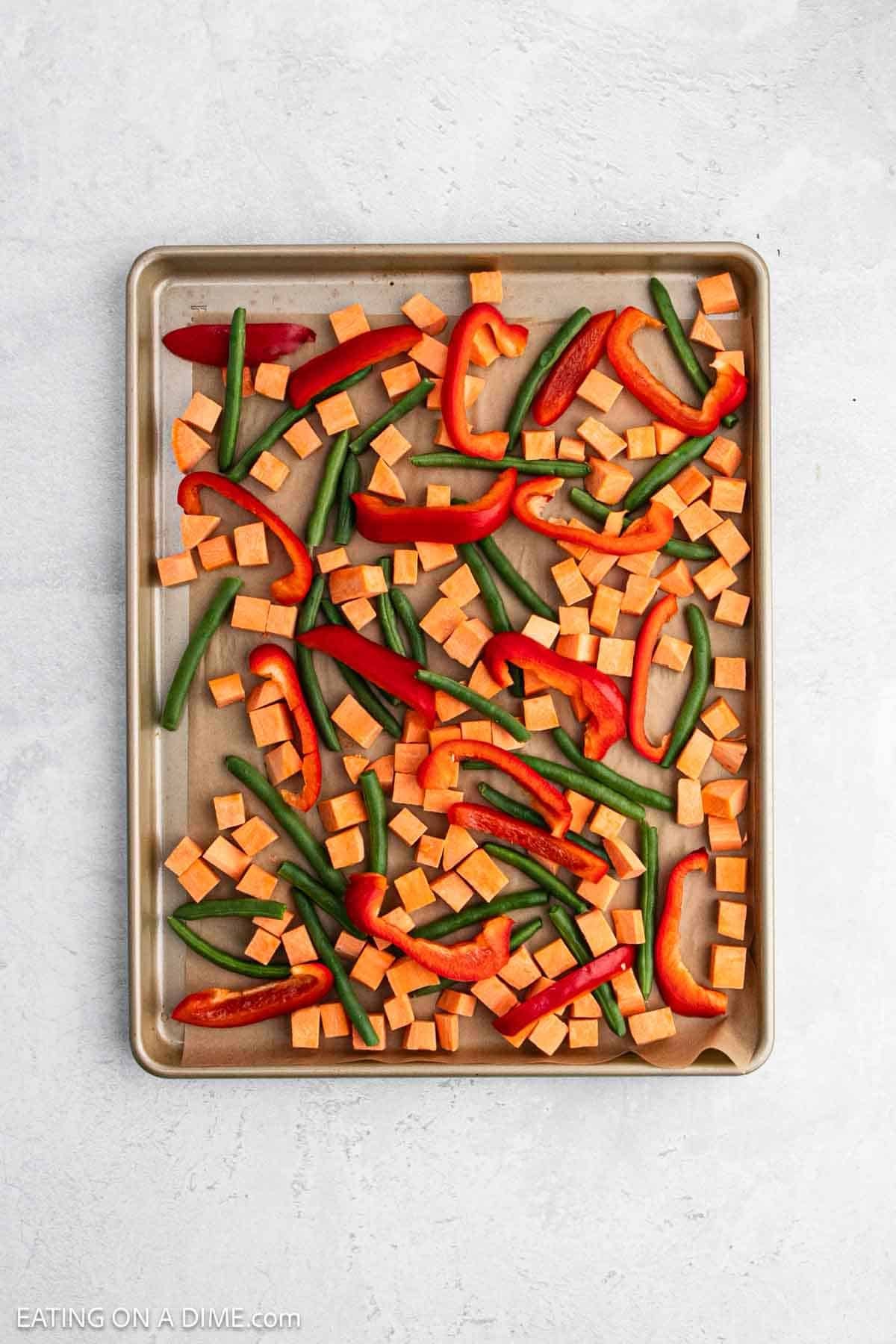 Diced sweet potatoes, green beans and slice bell peppers on a baking sheet.