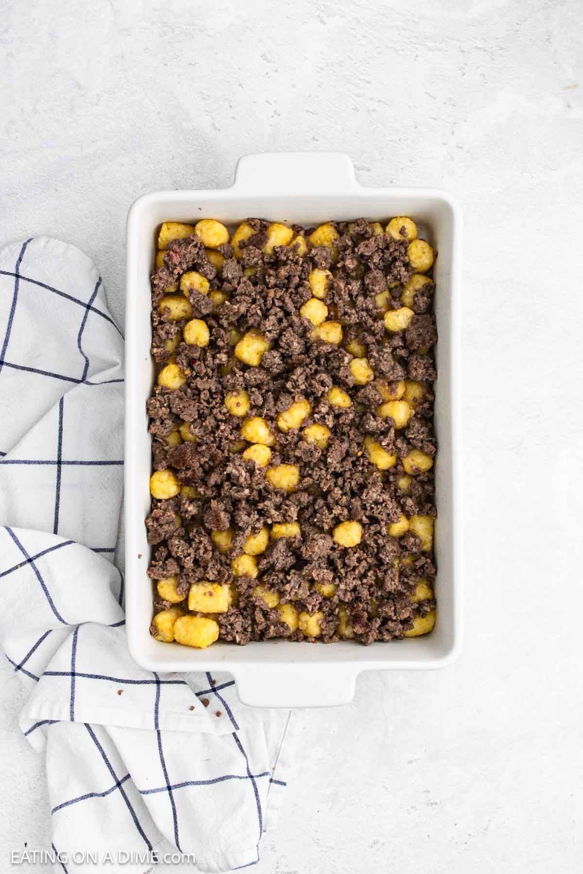 Sausage crumbles spread over tater tots in a baking dish.