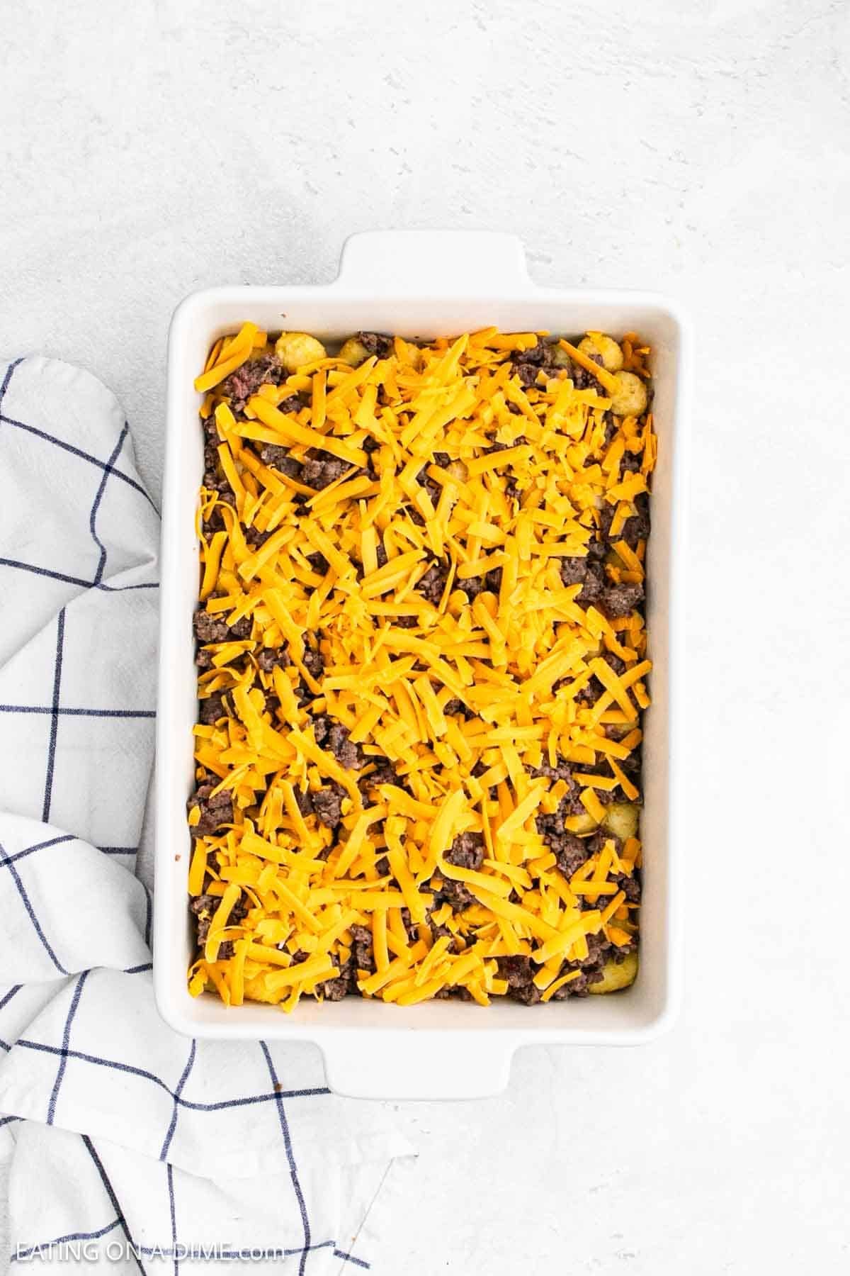 Shredded cheese spread over sausage and tater tots in the baking dish.
