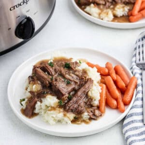 Shredded roast and gravy over mashed potatoes with a side of carrots on a plate.