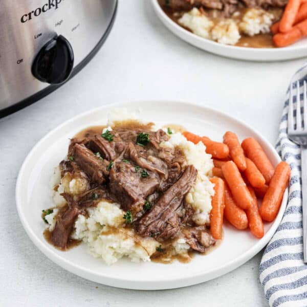 Shredded roast and gravy over mashed potatoes with a side of carrots on a plate.