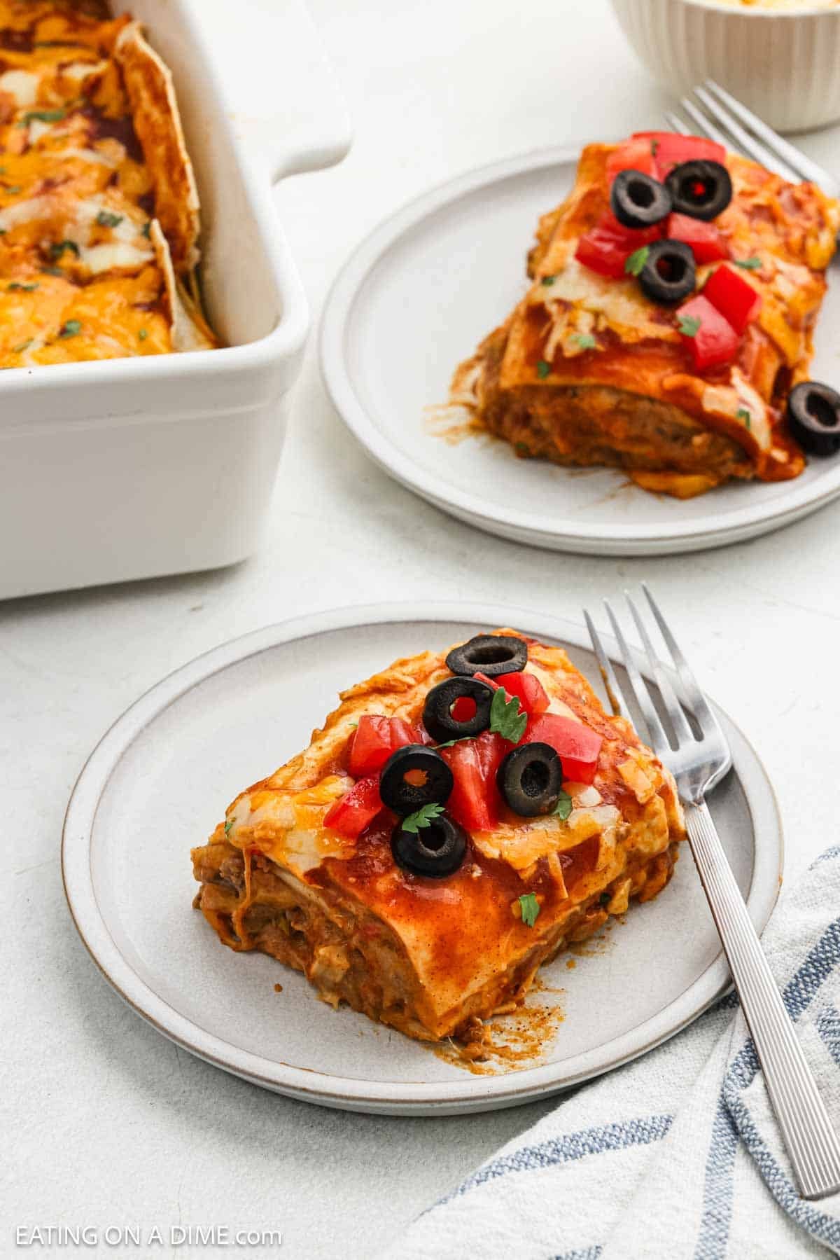 A serving of burrito casserole on a plate topped with diced tomatoes and black olives.