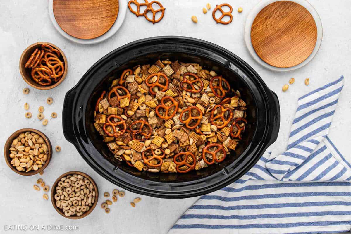 Slow Cooker Chex Mix with small bowls of cheerios, peanuts, and pretzels nearby.
