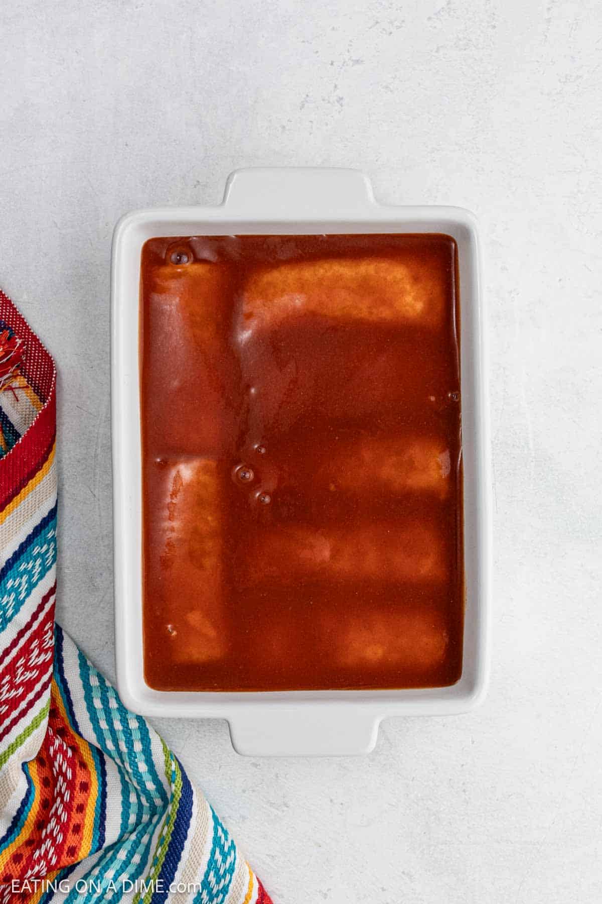 Topping the frozen burritos with enchilada sauce in the baking dish.