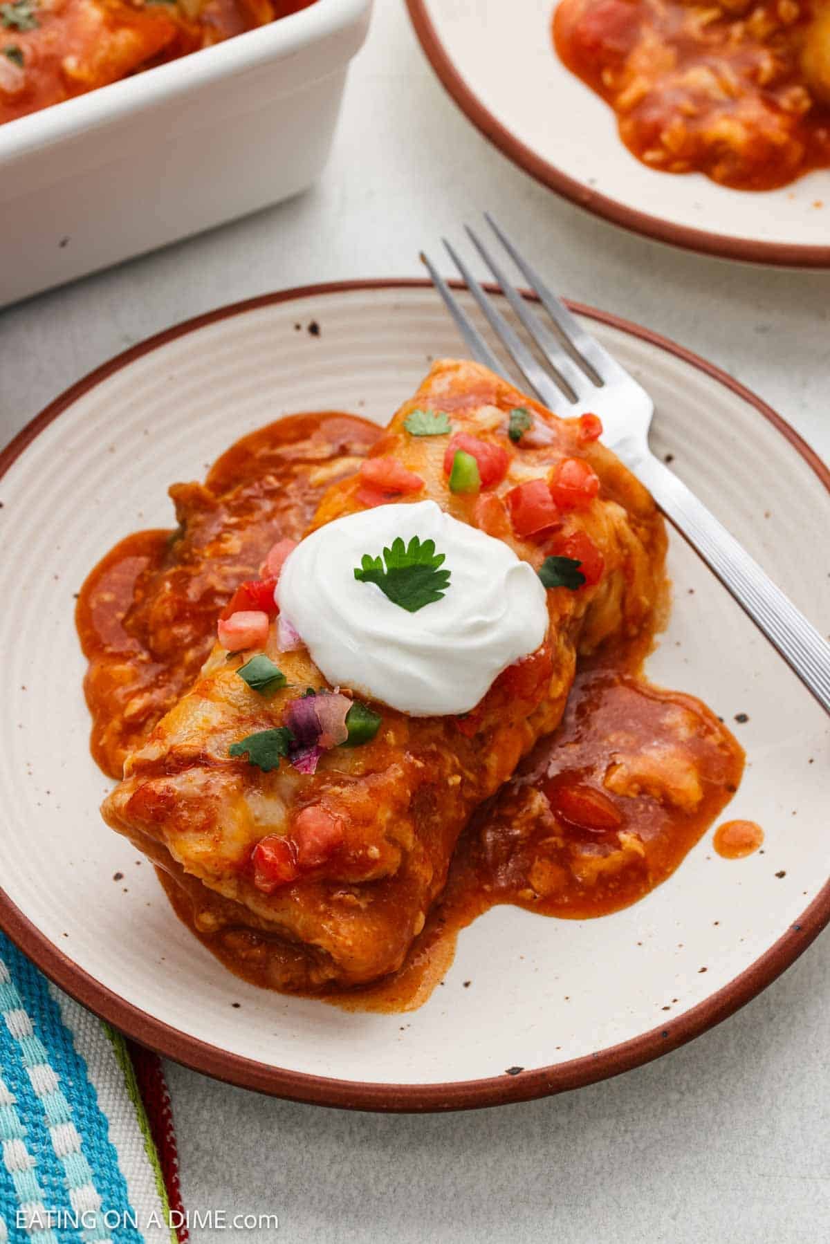 Burrito topped with enchilada sauce, sour cream and pico de gallo on a plate.