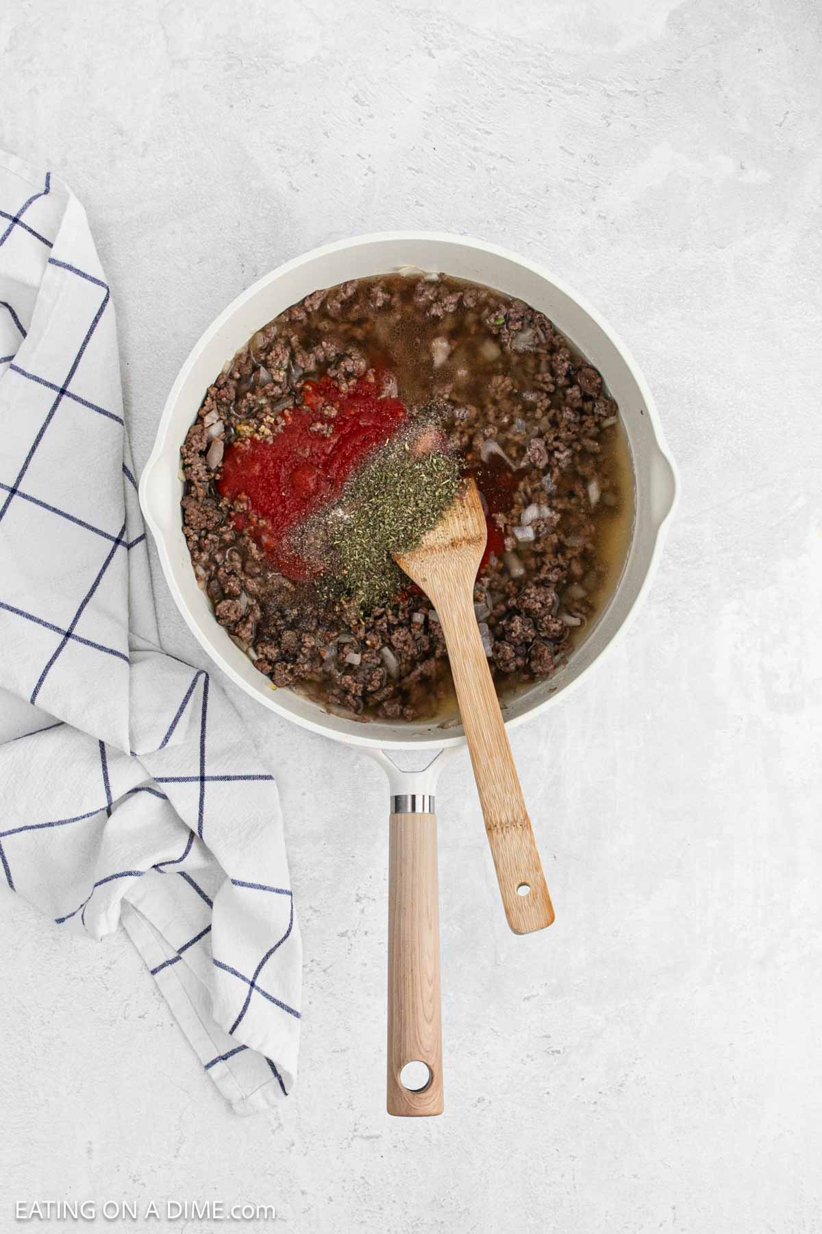 Cooked ground beef topped with broth, tomato sauce, and spices in a skillet.