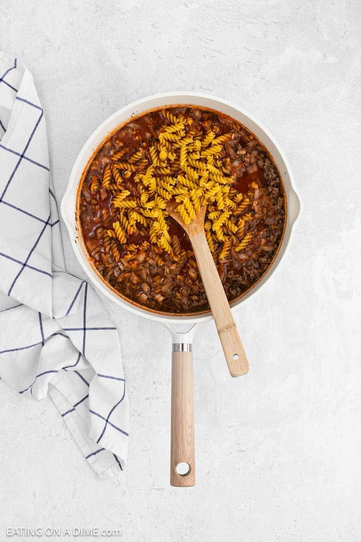 Rotini pasta mixed with the ground mixture in a skillet.
