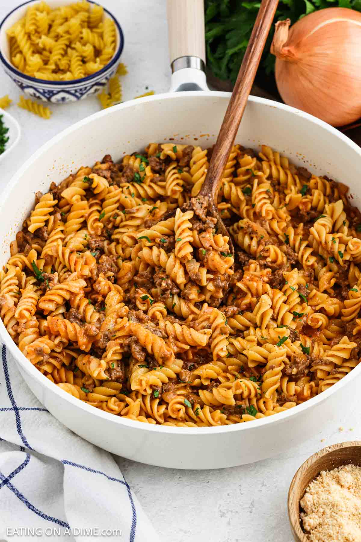 Ground beef and pasta mixed together in a large white bowl with a wooden spoon.