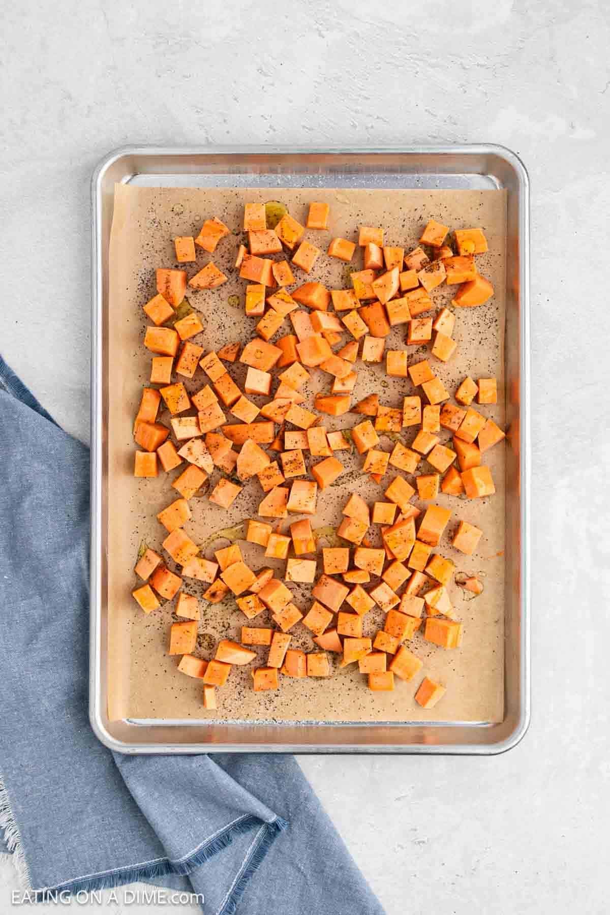 Diced potatoes on a baking sheet lined with parchment paper topped with spices.