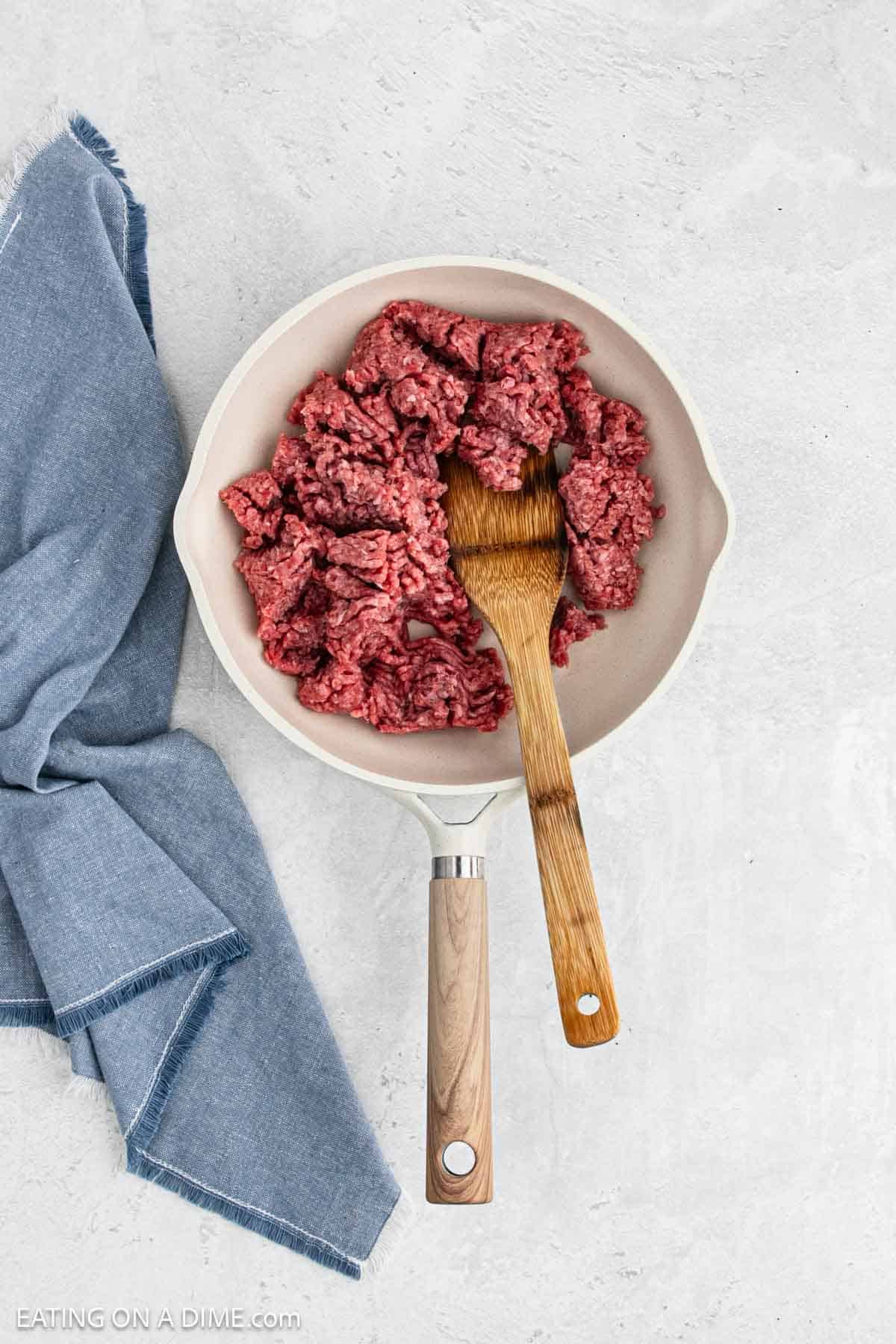 Cooking ground beef in a large skillet with a wooden spoon.