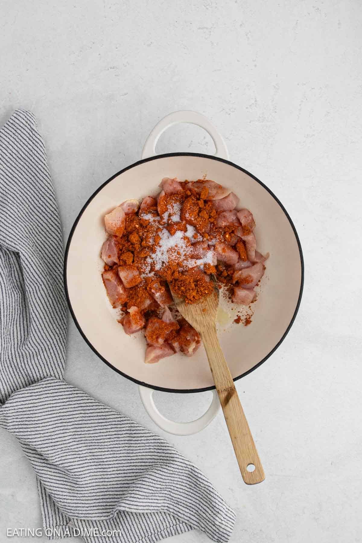 Cooking diced chicken topped with spices in a large pot with a wooden spoon.