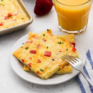 A servings of sheet pan eggs topped red bell pepper on a plate with a glass of orange juice nearby.