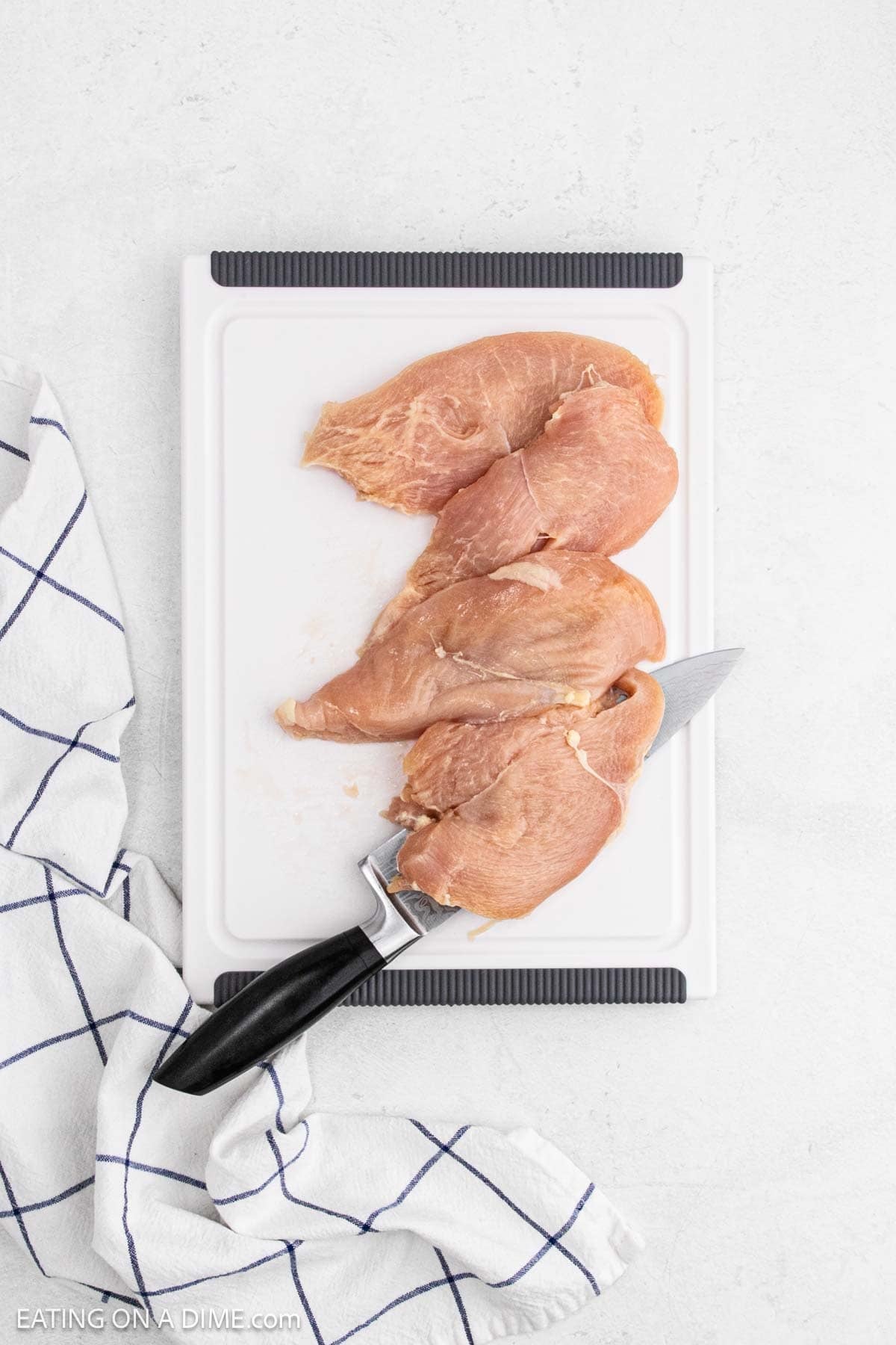 Slicing chicken breast on a cutting board with a knife.