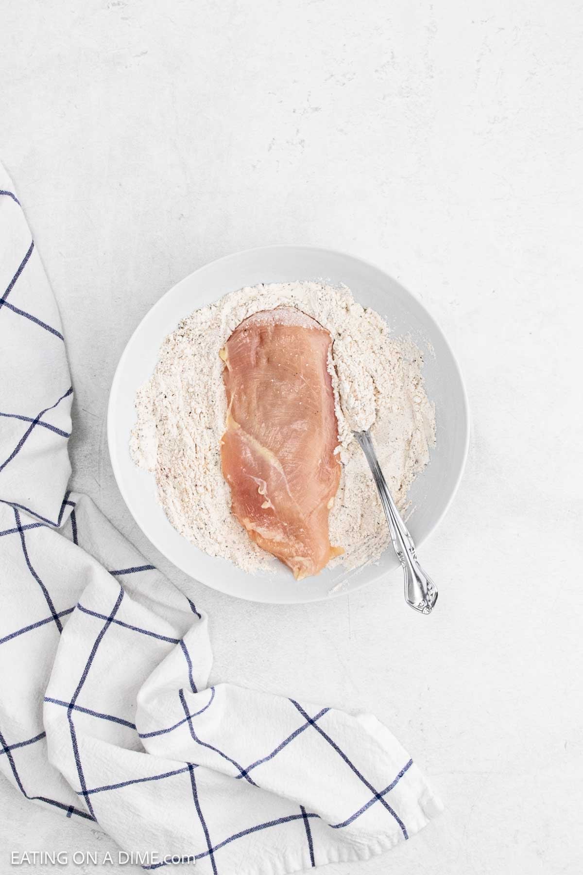 Placing chicken breast in the flour mixture in a bowl.