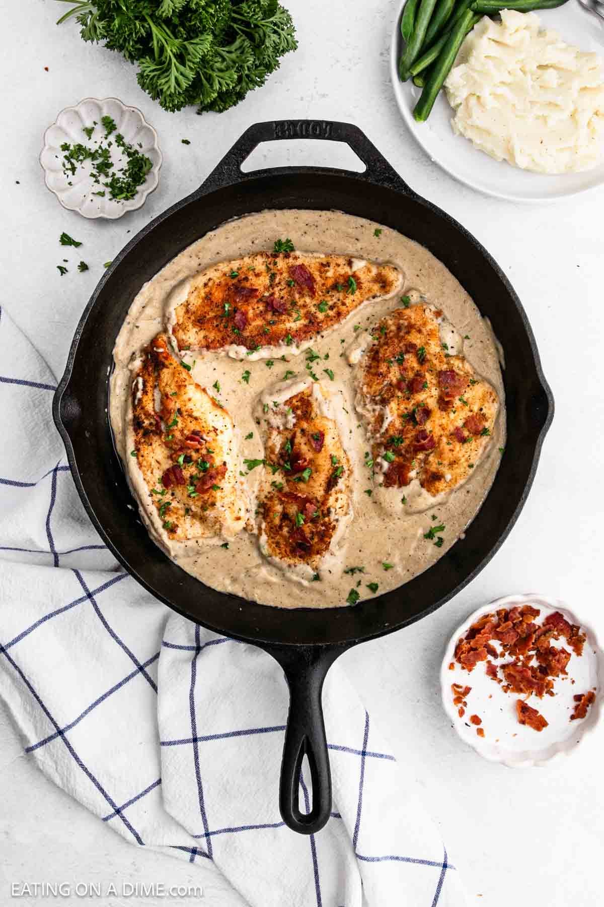 Golden brown chicken breast topped with bacon in a cast iron skillet with gravy.