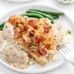 Smothered chicken on a plate with mashed potatoes and green beans.
