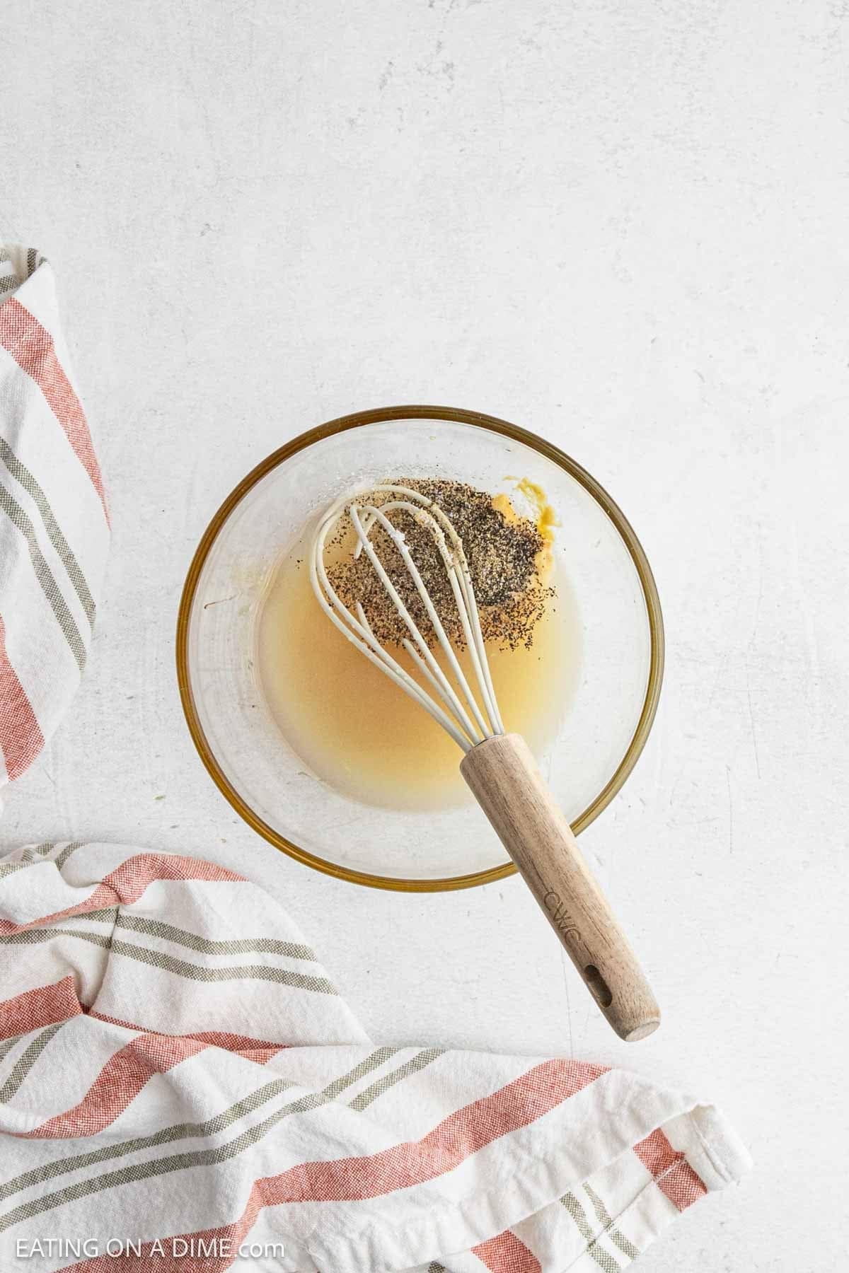 Dressing ingredients in a bowl with a whisk.
