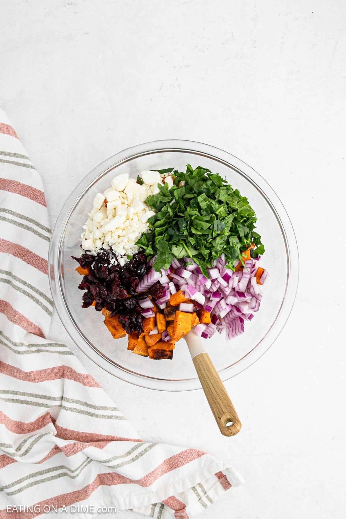 Roasted sweet potatoes in a bowl topped with feta cheese, spinach, cranberries, and red onion.