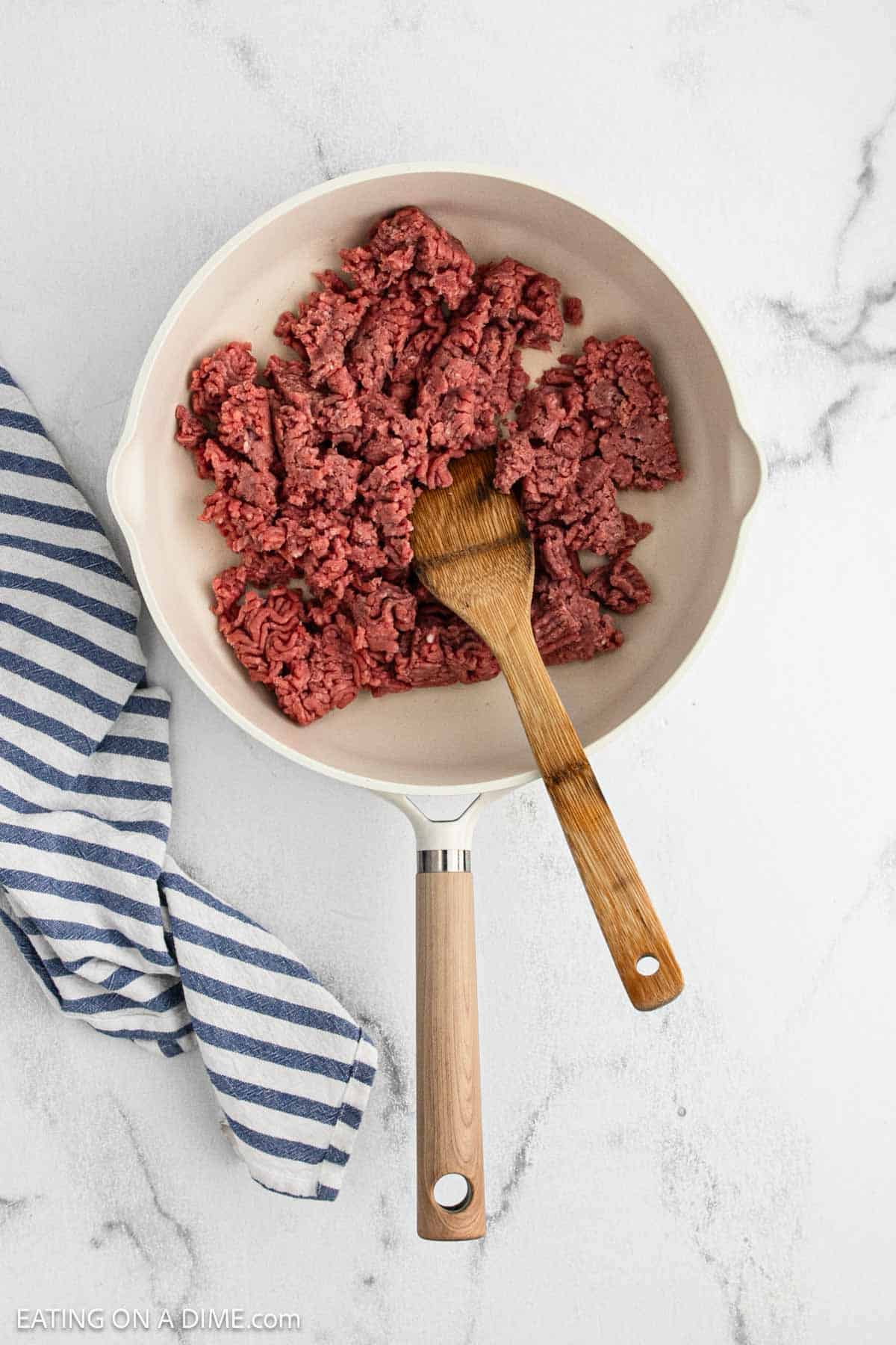 Cooking ground beef in a large skillet with a wooden spoon.