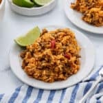A serving of taco rice on a plate with a side of lime wedge.