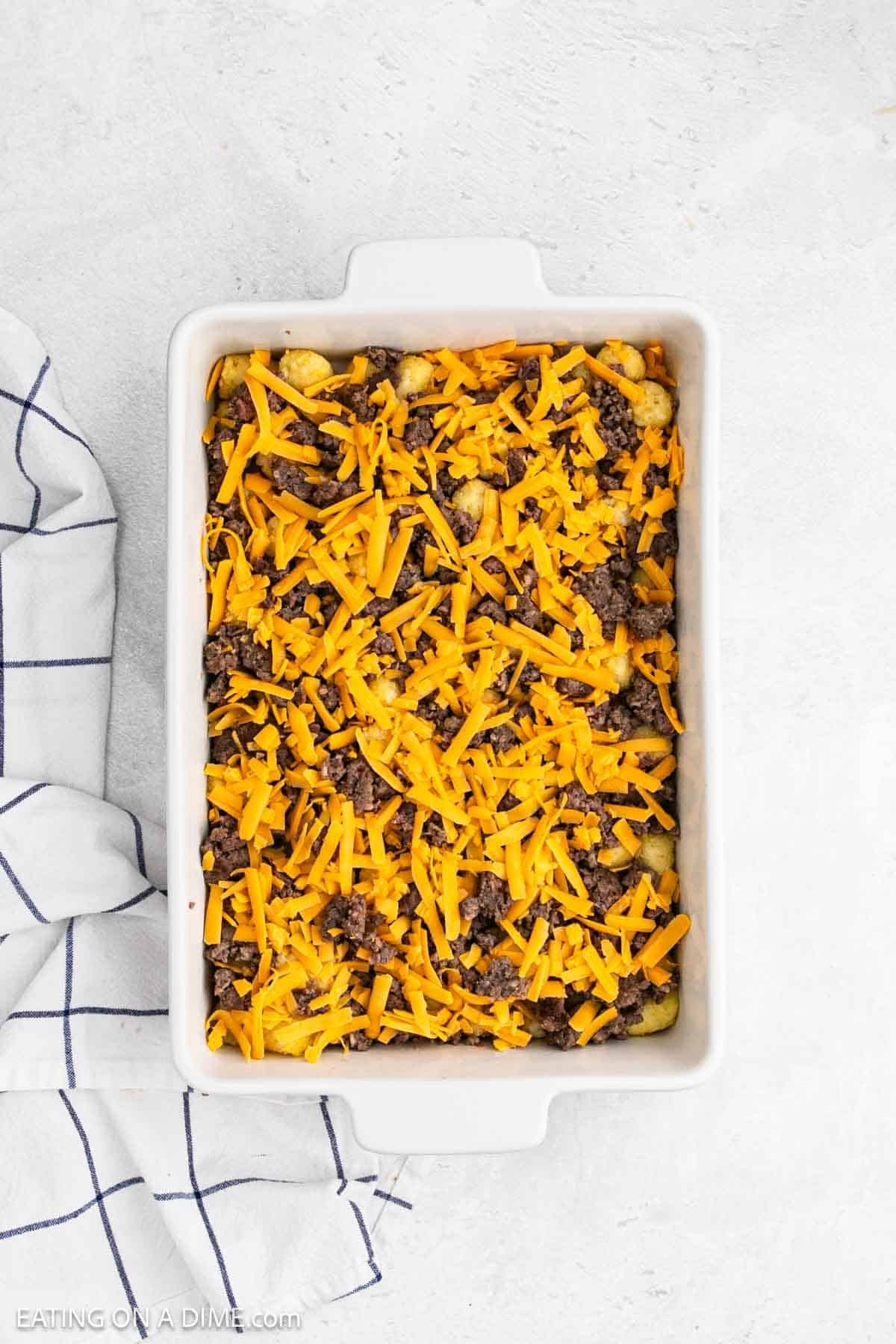 Egg mixture poured over the shredded cheese, tater tots, and sausage crumbles in the baking dish.