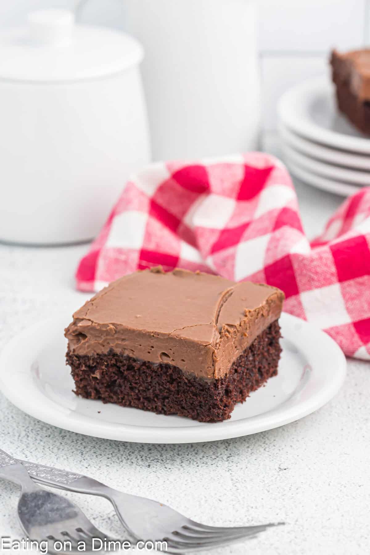 A slice of chocolate cake topped with thick chocolate frosting on a plate.