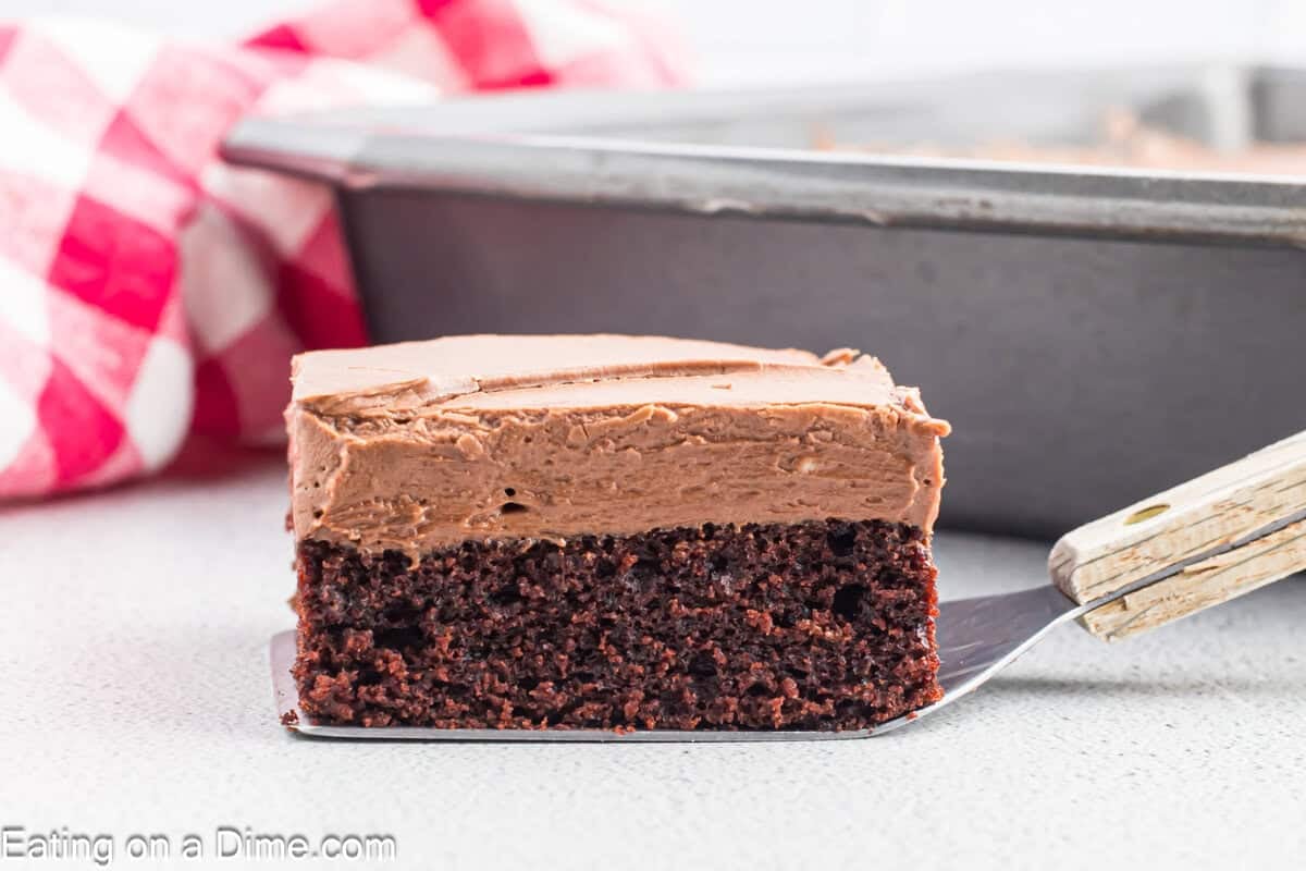 A slice of chocolate cake with thick chocolate frosting on a spatula. 