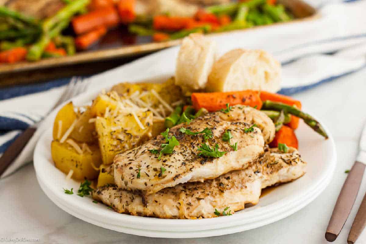 Balsamic chicken breast stacked on a plate with a side of roasted potatoes, carrots and asparagus. 